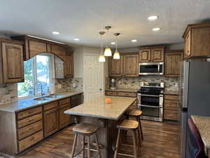 Kitchen with appliances with stainless steel finishes, hanging light fixtures, dark wood-style floors, a kitchen bar, and backsplash