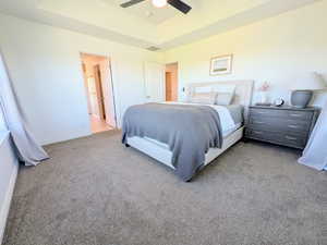Bedroom featuring a tray ceiling, light carpet, and a ceiling fan