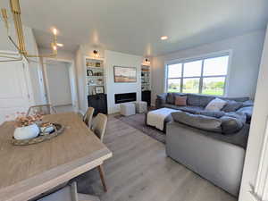 Living room with a large fireplace, a chandelier, light wood-style floors, built in features, and recessed lighting