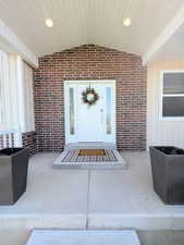 Doorway to property with board and batten siding, brick siding, and a patio