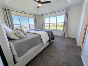 Carpeted bedroom with a tray ceiling and ceiling fan