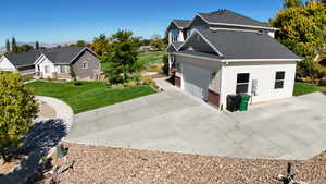View of side of home featuring a shingled roof, a lawn, a garage, and concrete driveway