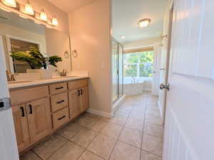 Bathroom featuring double vanity, light tile patterned flooring, a garden tub, and a stall shower