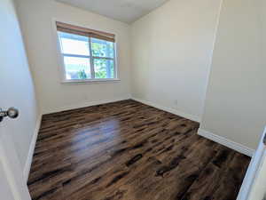 Spare room featuring dark wood-style flooring and baseboards