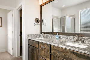 Full bathroom with a shower stall, double vanity, light wood finished floors, and a walk in closet