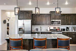 Kitchen with dark brown cabinetry, a kitchen bar, stainless steel appliances, light stone countertops, and recessed lighting