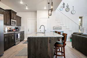 Kitchen featuring dark brown cabinetry, a breakfast bar area, stainless steel appliances, light stone counters, and recessed lighting