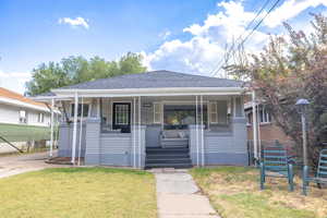 Bungalow-style home with covered porch, roof with shingles, and a front yard