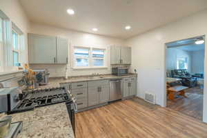 Kitchen featuring gray cabinetry, appliances with stainless steel finishes, light wood-type flooring, recessed lighting, and light stone counters