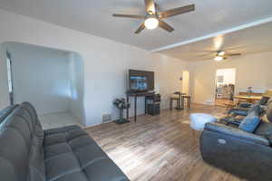 Living area with light wood finished floors, a ceiling fan, a textured ceiling, arched walkways, and beam ceiling