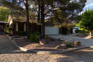 View of property hidden behind natural elements featuring driveway, a garage, and brick siding