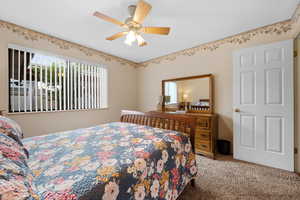 Carpeted bedroom featuring multiple windows and ceiling fan