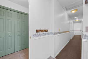 Corridor featuring a wainscoted wall, attic access, and stone tile floors