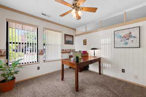 Office featuring wooden walls, carpet flooring, a textured ceiling, a ceiling fan, and ornamental molding