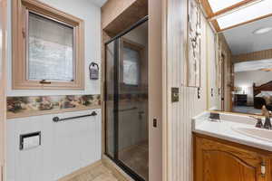 Bathroom featuring a shower stall, vanity, ensuite bathroom, wainscoting, and wallpapered walls