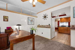 Office area with ornamental molding, a ceiling fan, light carpet, a tray ceiling, and light stone finish floors
