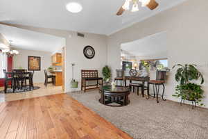 Living area featuring light wood-style flooring, lofted ceiling, a chandelier, and a ceiling fan
