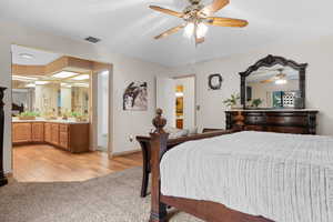 Bedroom featuring light carpet, ensuite bath, ceiling fan, and light wood finished floors