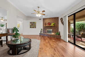 Living room with a ceiling fan, light wood-style floors, vaulted ceiling, and a fireplace