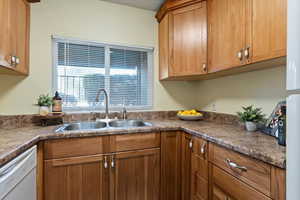 Kitchen with brown cabinets, dishwasher, and dark countertops