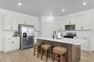 Kitchen with appliances with stainless steel finishes, light wood-style flooring, a kitchen island with sink, a kitchen bar, and recessed lighting