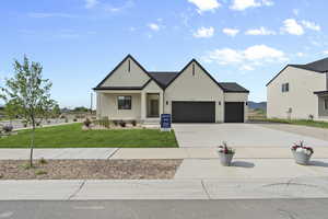 Modern farmhouse style home featuring concrete driveway, stucco siding, a front lawn, an attached garage, and covered porch