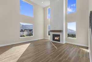 Unfurnished living room with a towering ceiling, a large fireplace, wood finished floors, and plenty of natural light