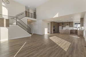 Unfurnished living room featuring a high ceiling, stairway, recessed lighting, and dark wood-style flooring
