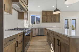 Kitchen featuring stainless steel appliances, custom range hood, light stone counters, decorative light fixtures, and recessed lighting