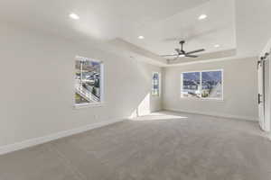 Unfurnished room with a barn door, a tray ceiling, carpet floors, recessed lighting, and a ceiling fan