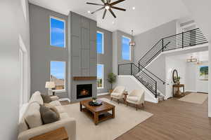 Living room with a towering ceiling, wood finished floors, a chandelier, a large fireplace, and stairs