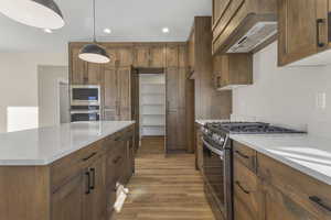 Kitchen with appliances with stainless steel finishes, brown cabinets, a kitchen island, recessed lighting, and custom exhaust hood