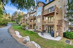 Back of property with a lawn, stone siding, a patio area, a balcony, and french doors