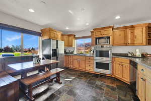 Kitchen featuring stainless steel appliances, stone tile flooring, recessed lighting, open shelves, and dark stone counters