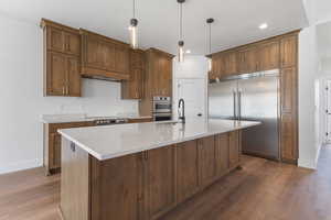 Kitchen with stainless steel appliances, pendant lighting, light stone countertops, light wood-style flooring, and an island with sink