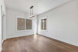 Unfurnished dining area featuring wood finished floors and a chandelier