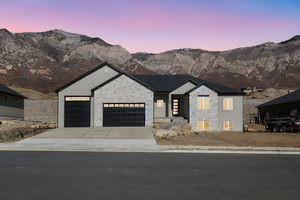 View of front facade with a mountain view, stone siding, a garage, and concrete driveway