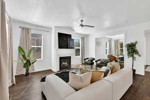 Living room with a textured ceiling, a ceiling fan, dark wood-type flooring, a glass covered fireplace, and recessed lighting
