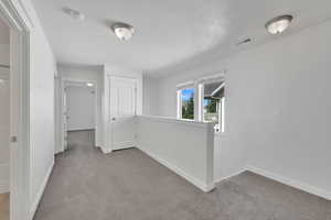 Hallway featuring light carpet, an upstairs landing, and a textured ceiling