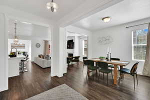 Dining area with dark wood-style floors, a lit fireplace, and a chandelier