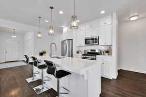 Kitchen with a breakfast bar area, decorative backsplash, white cabinetry, decorative light fixtures, and stainless steel appliances