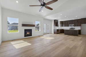 Unfurnished living room with recessed lighting, vaulted ceiling, light wood-type flooring, a glass covered fireplace, and ceiling fan