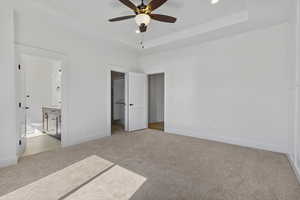 Unfurnished bedroom featuring light colored carpet, a walk in closet, a raised ceiling, ensuite bath, and recessed lighting