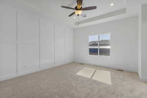 Unfurnished bedroom featuring a tray ceiling, ceiling fan, light colored carpet, a decorative wall, and recessed lighting