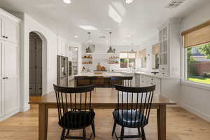 Kitchen featuring a center island, white cabinets, arched walkways, pendant lighting, and light wood-style floors