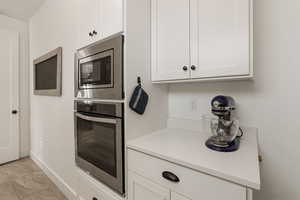 Kitchen with stainless steel appliances, white cabinets, and light stone countertops