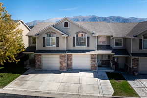View of front facade with stone siding, a mountain view, an attached garage, and driveway