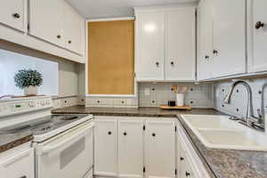 Kitchen featuring white range with electric cooktop, dark countertops, white cabinetry, and backsplash