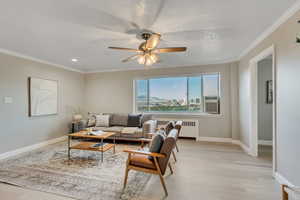 Living area with ornamental molding, light wood finished floors, ceiling fan, radiator, and recessed lighting