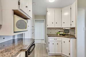 Kitchen with tasteful backsplash, white microwave, white cabinetry, and a textured ceiling